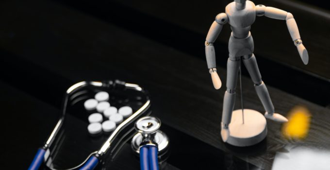 Pills, a stethoscope and a fake person on a black background