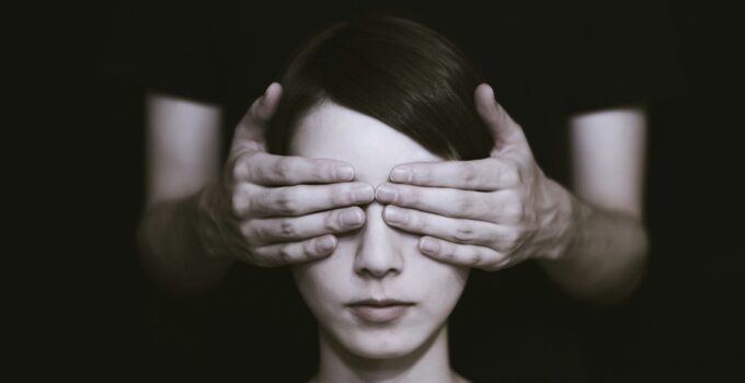 person covering the eyes of woman on dark room